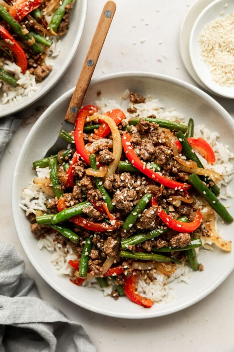 Overhead view of a plate of ground beef stir fry on top of rice and topped with sesame seeds. 