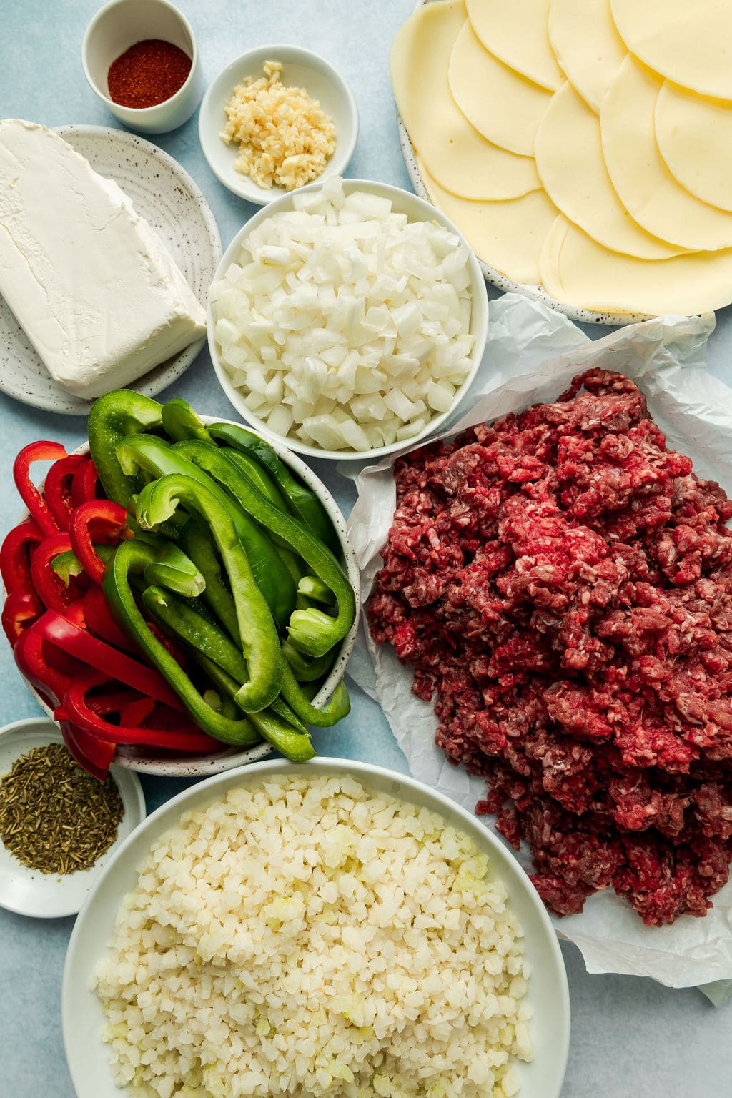 Overhead view of variety of ingredients arranged in white bowls for Low Carb Philly Cheesesteak Casserole. 