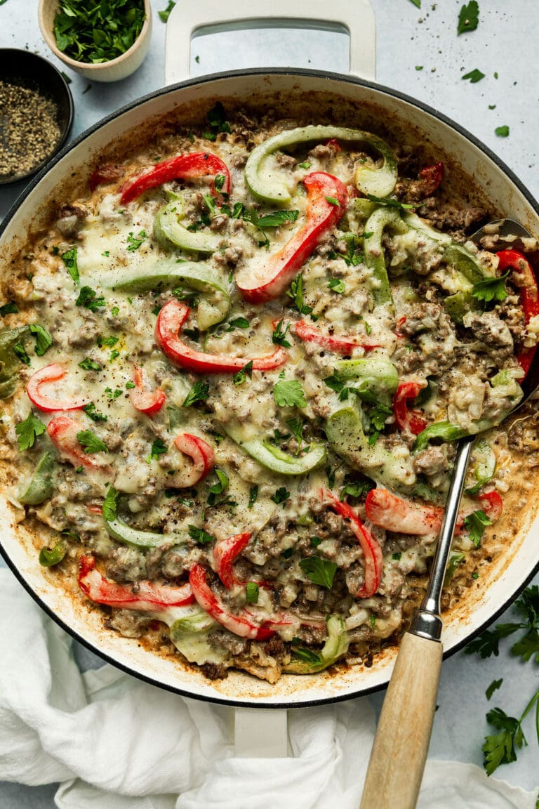 Overhead view of a skillet filled with Philly cheesesteak casserole topped with melted provolone cheese, and fresh herbs. 