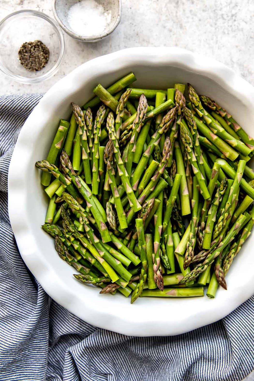 Pie pan filled with chopped asparagus next to small bowls of salt and pepper. 