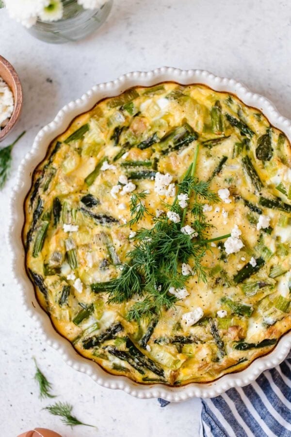 Overhead view white pie plate filled with crustless quiche with asparagus, leek and feta