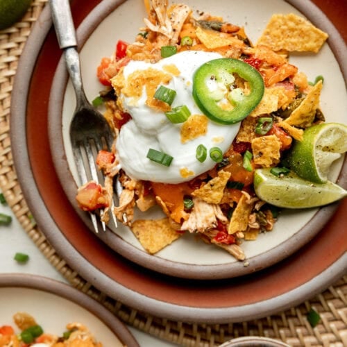 Close up view of plated King Ranch Chicken Casserole topped with a dollop of sour cream and sliced jalapeno and green onions.