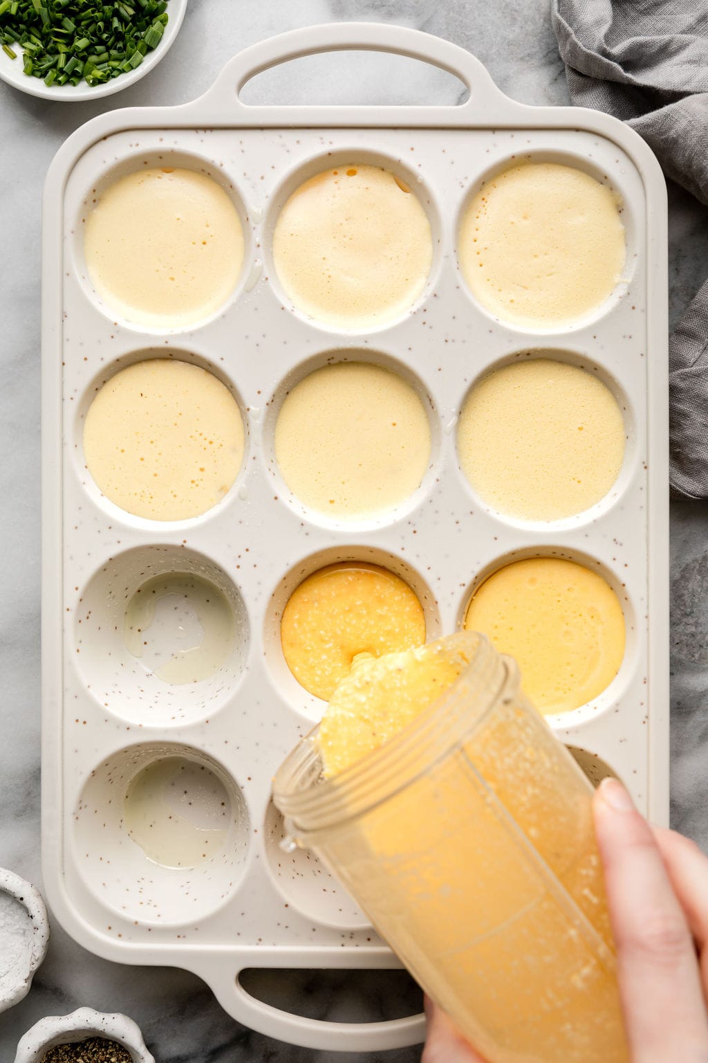 Overhead view of egg bites mixture being poured into muffin pan wells. 