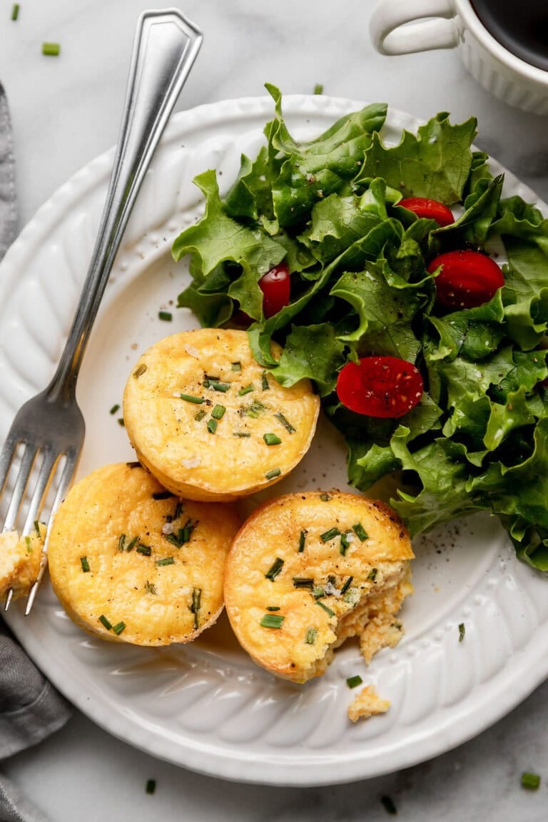 Overhead view of a plate filled with fresh greens and egg bites topped with fresh chives.