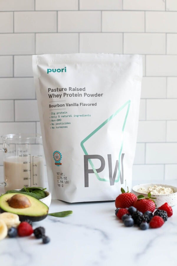 A bag of puori protein powder next to fresh fruits on a white countertop.