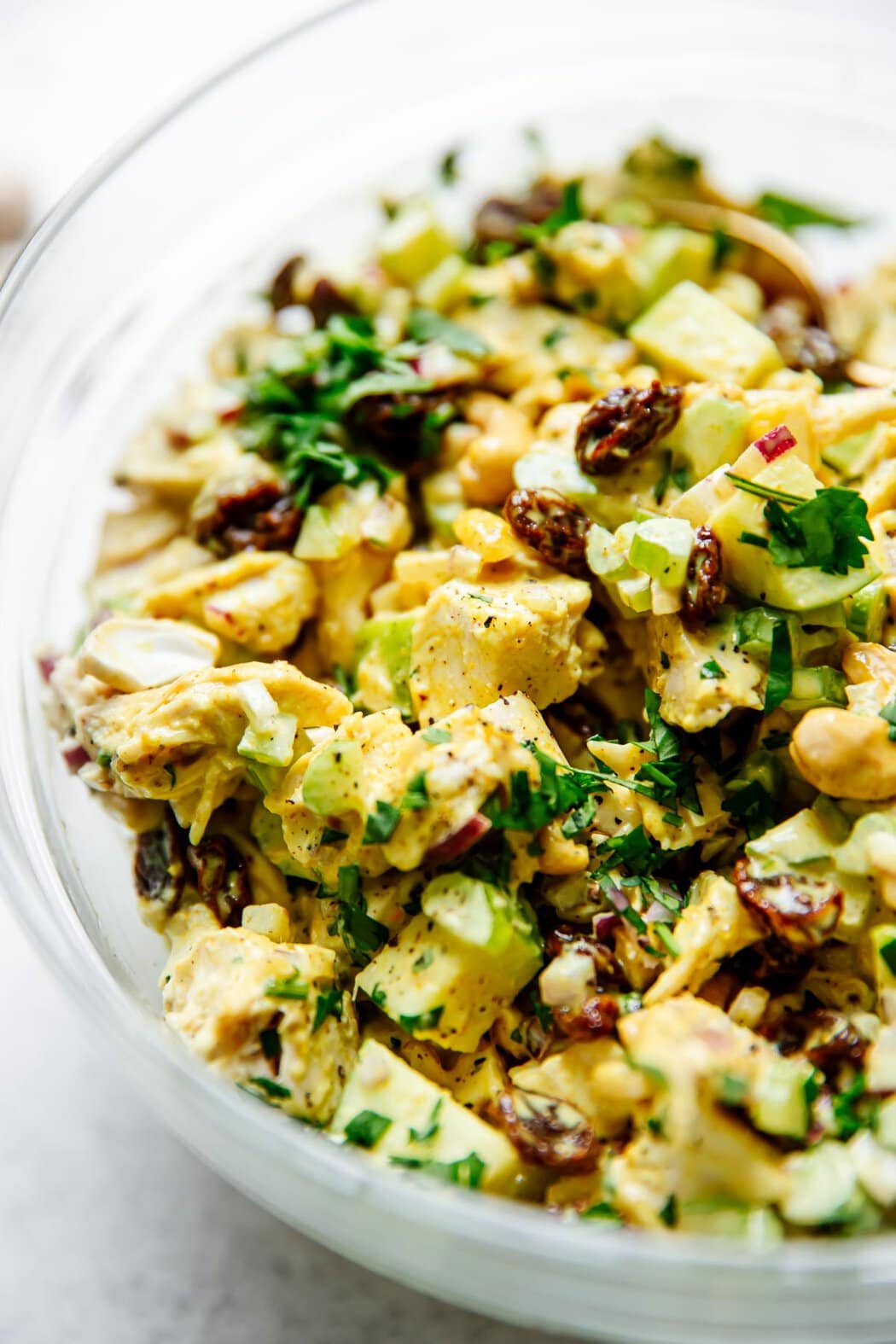 Close up view of a glass bowl filled with Curry Chicken Salad and topped with fresh cilantro and black pepper
