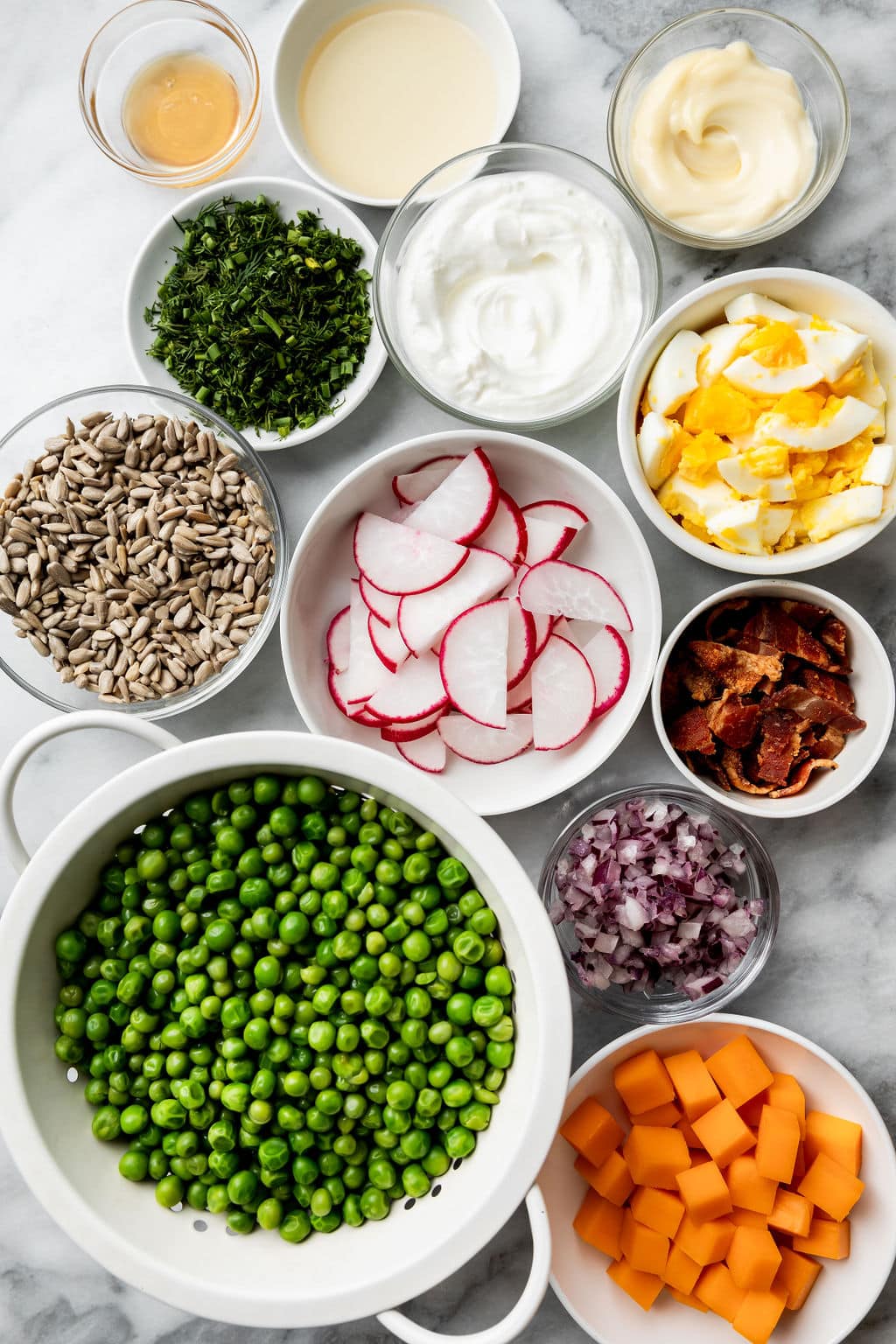 Overhead view of a variety of ingredients for Creamy Pea Salad in different sized bowls