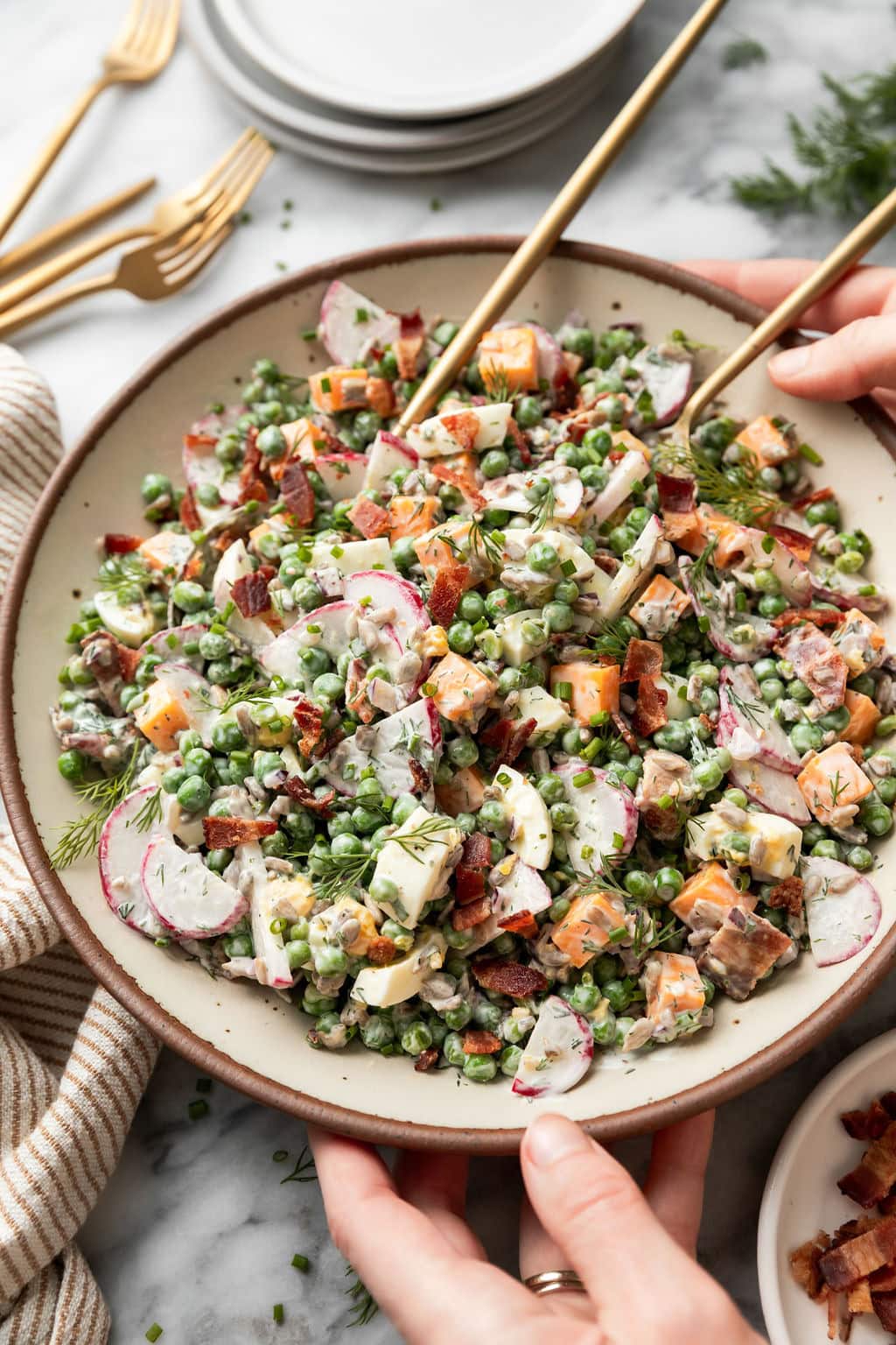 Close up view of a bowl of Creamy Pea Salad topped with fresh dill and bacon pieces