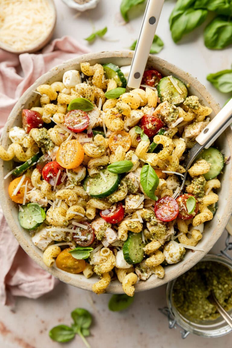 Overhead view of a large bowl of chicken pesto pasta salad topped with fresh basil. 