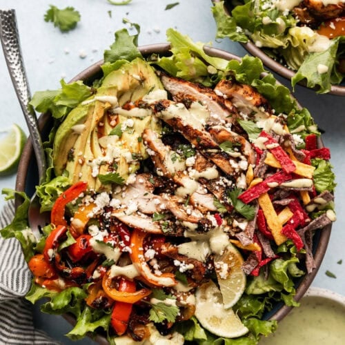 Overhead view large chicken fajita salad in bowl topped with cotija cheese and avocado lime sauce.