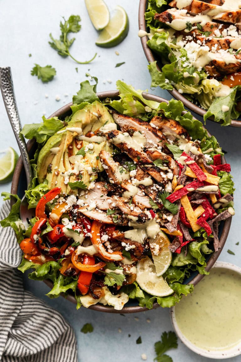 Overhead view of a grilled chicken fajita salad topped with colorful tortilla strips and garnished with lime wedges. 