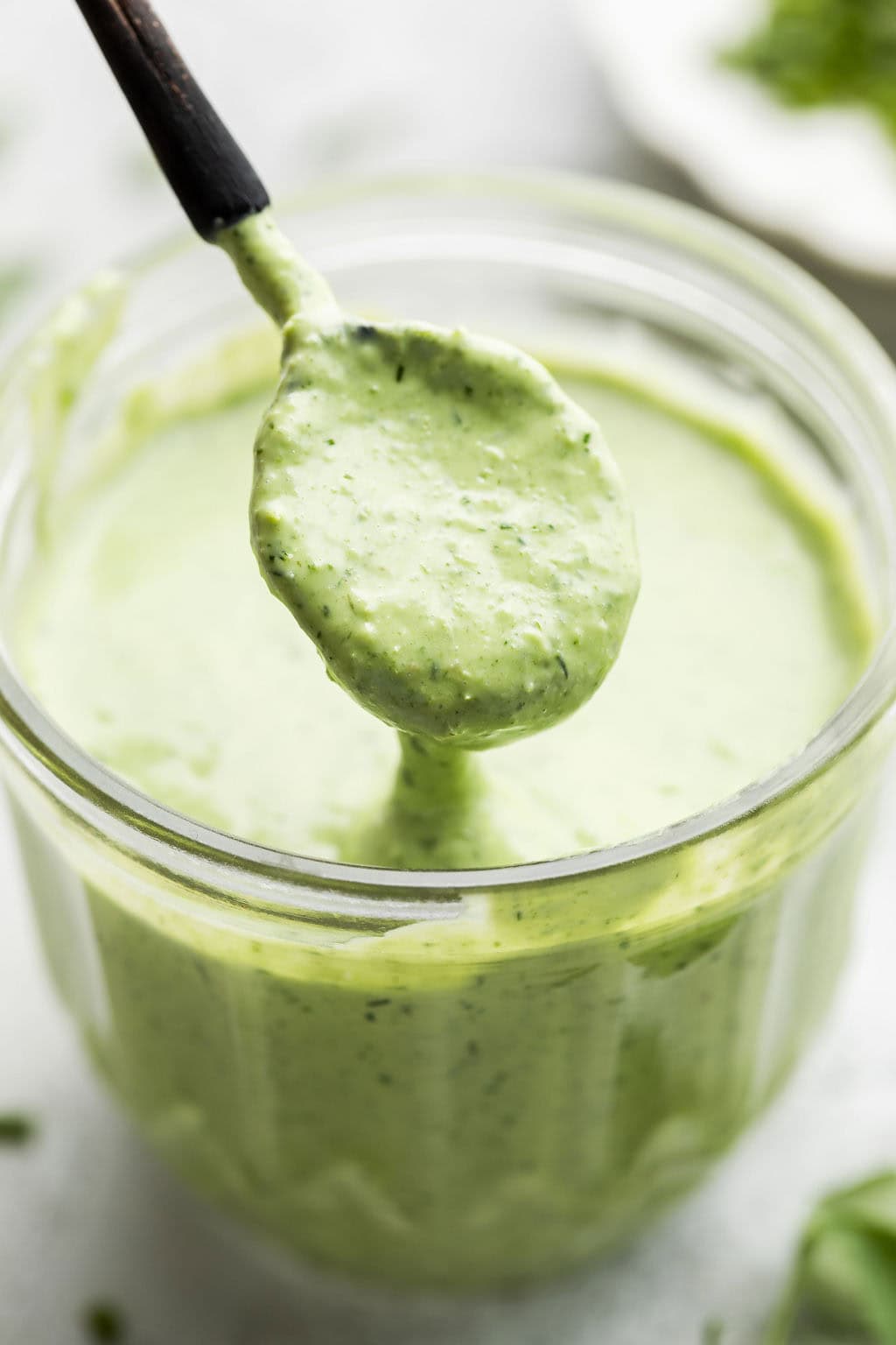 A spoon coming out of a bowl of fresh green goddess salad dressing.