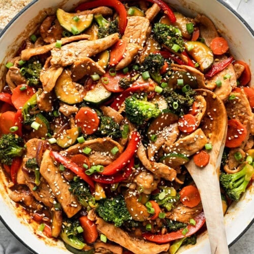 Overhead view skillet filled with orange pork stir fry sprinkled with sesame seeds