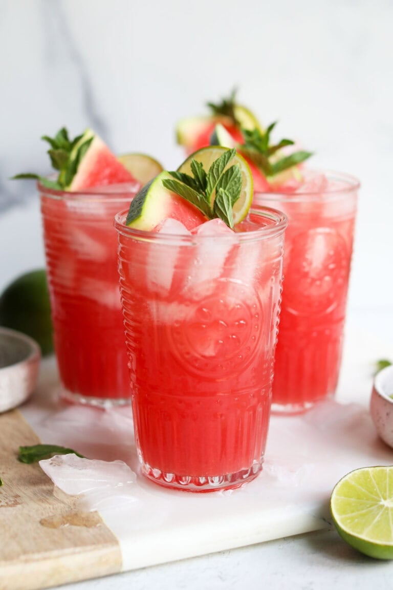 Close up view of watermelon lime mocktails in glasses garnished with watermelon wedges and fresh mint leaves.