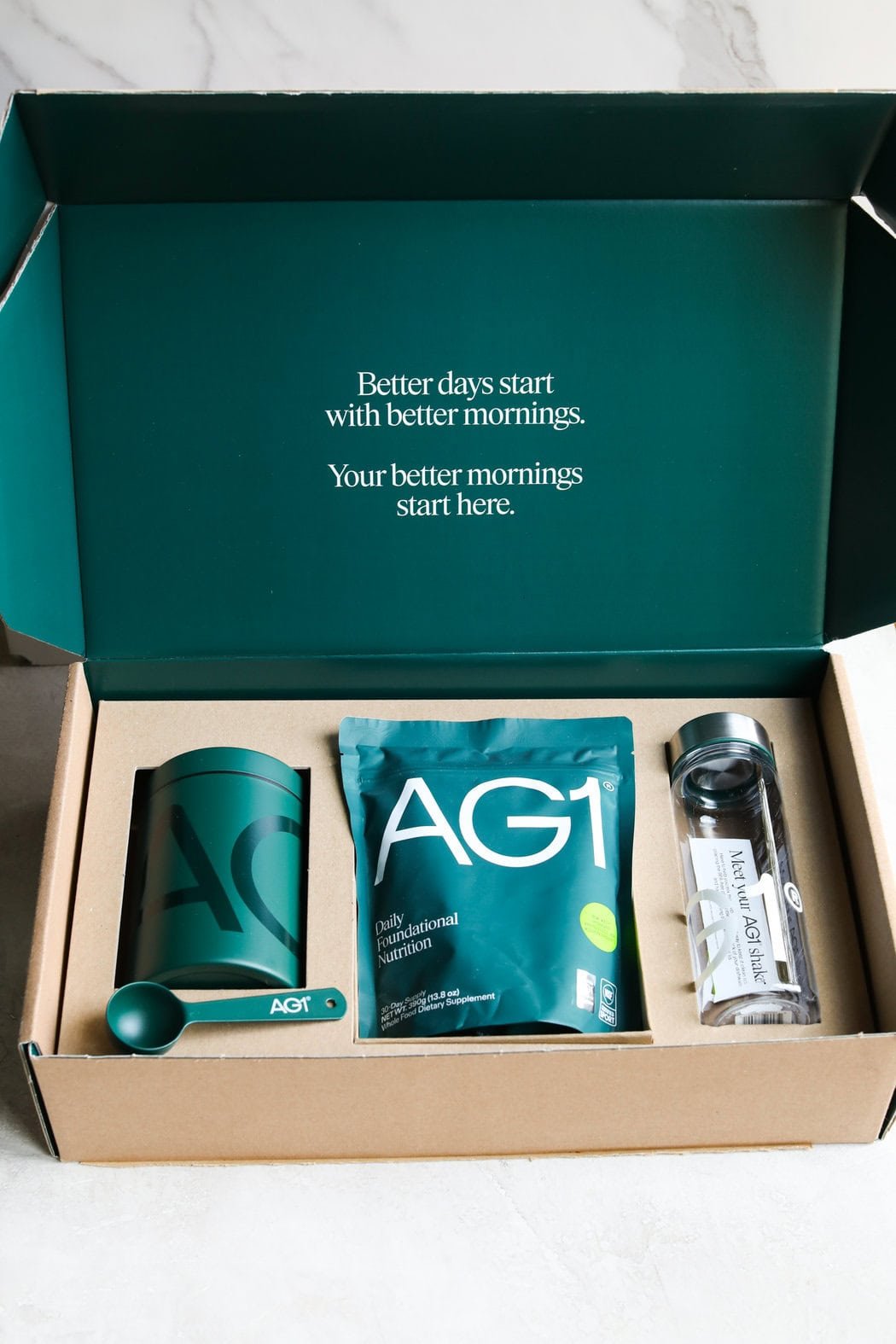 Close up view of a newly opened box of AG1 including the shaker bottle and storage canister in the packaging. 