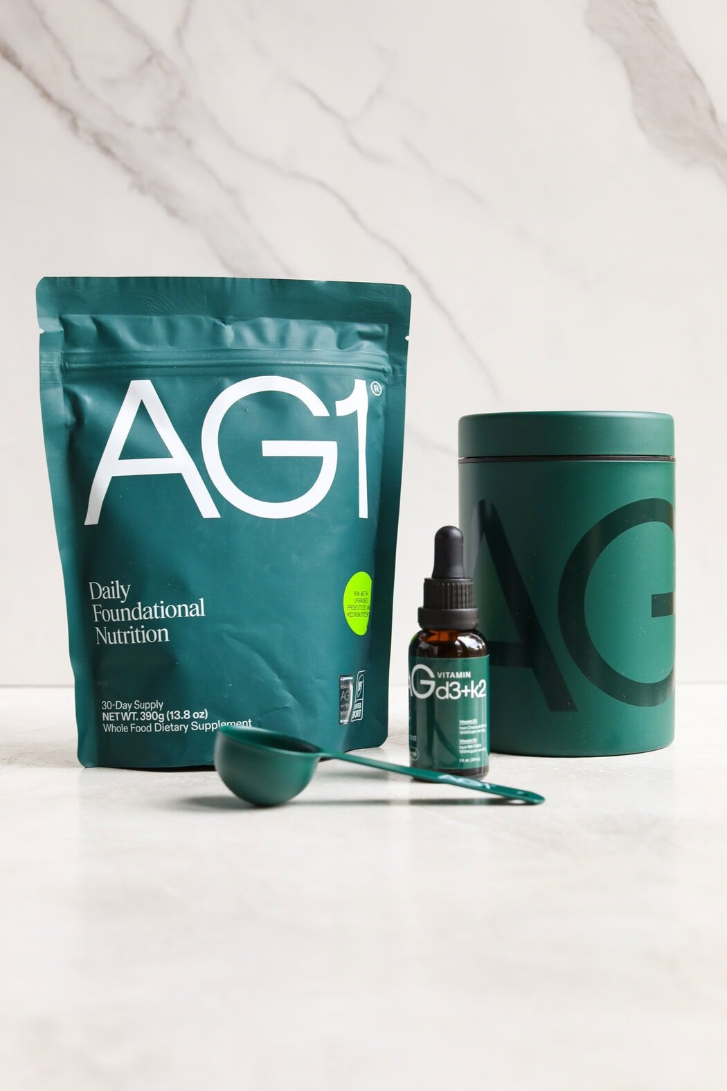 Close up view showing AG1 packaging and products on a white marble countertop. 