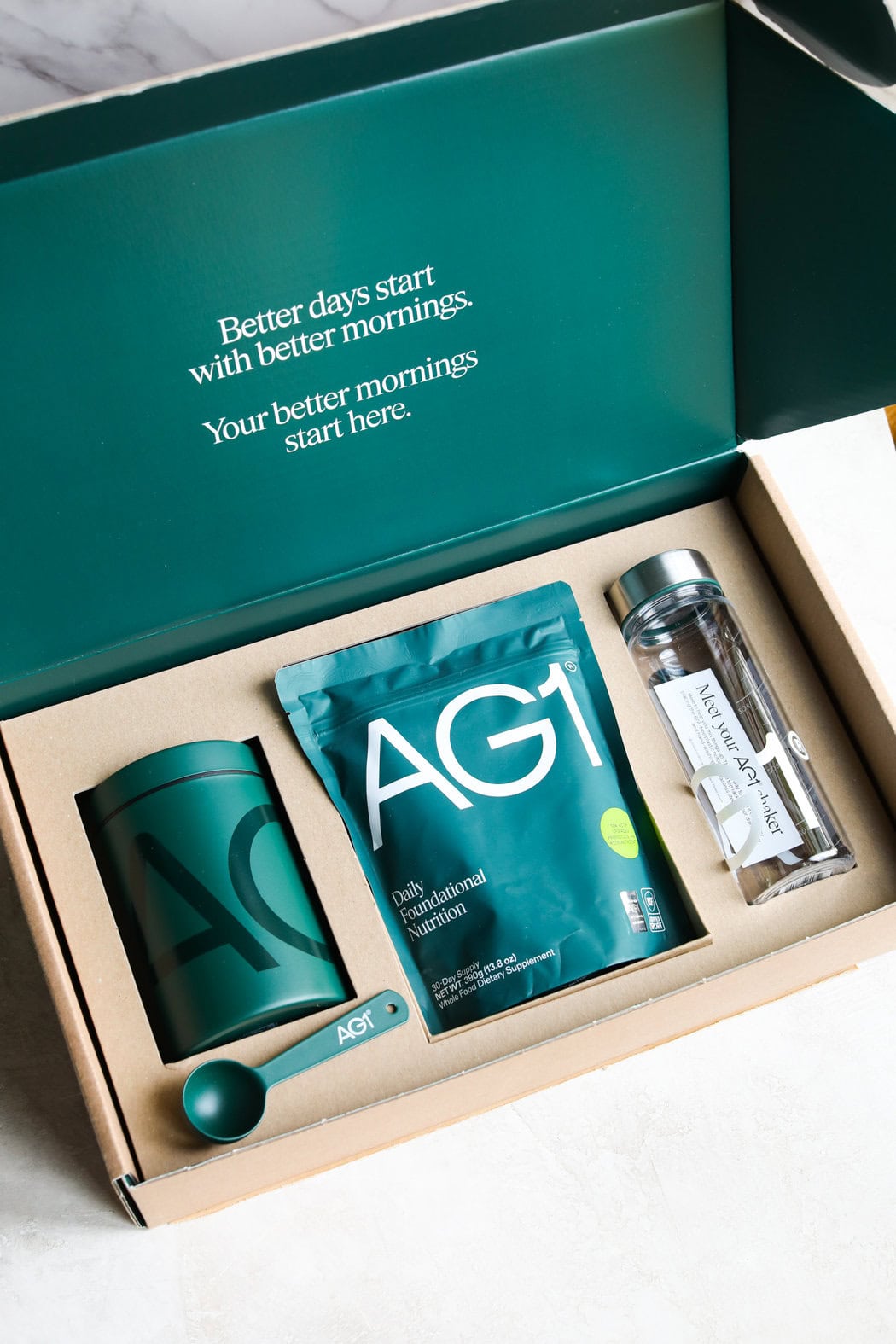 Overhead view of a box of AG1 greens showing the packaging and container with measuring spoon. 