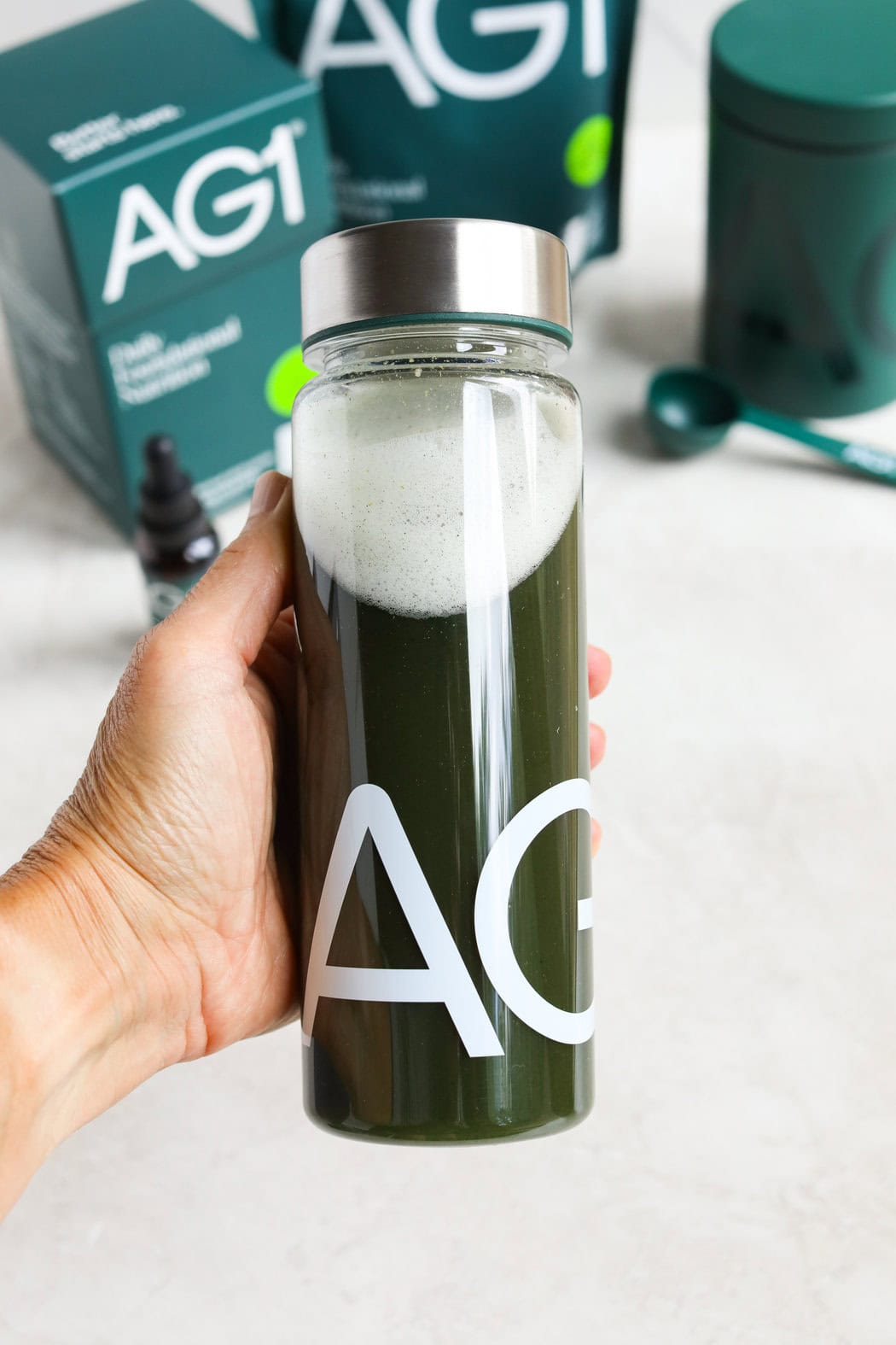 Close up view of a hand holding a clear bottle of AG1 greens mixed in water. 