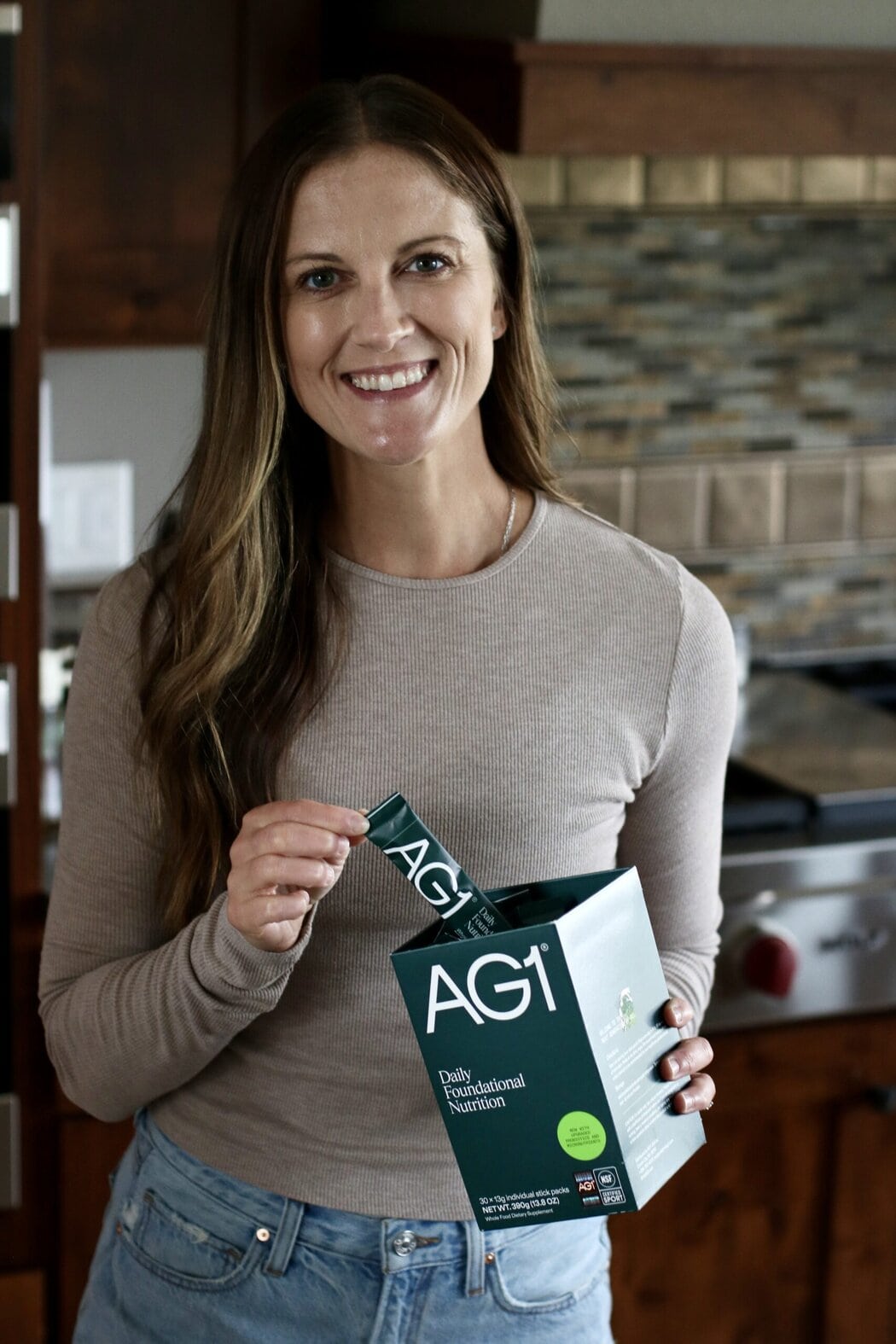 Close up view of a woman in a kitchen holding a box of travel AG1 sticks out of the box. 