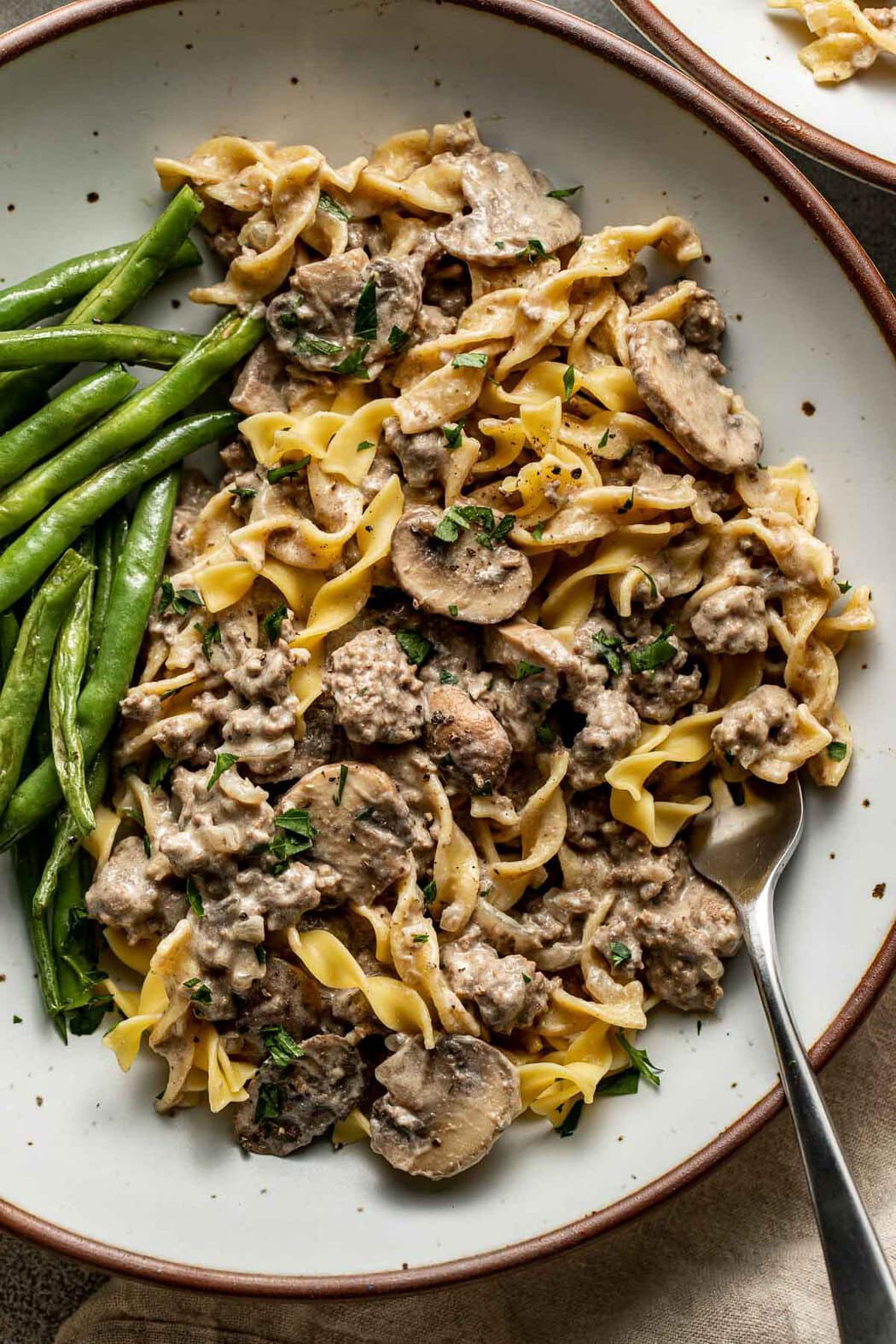 Overhead view of Easy and Delicious Ground Beef Stroganoff on a plate with green beans on the side. 
