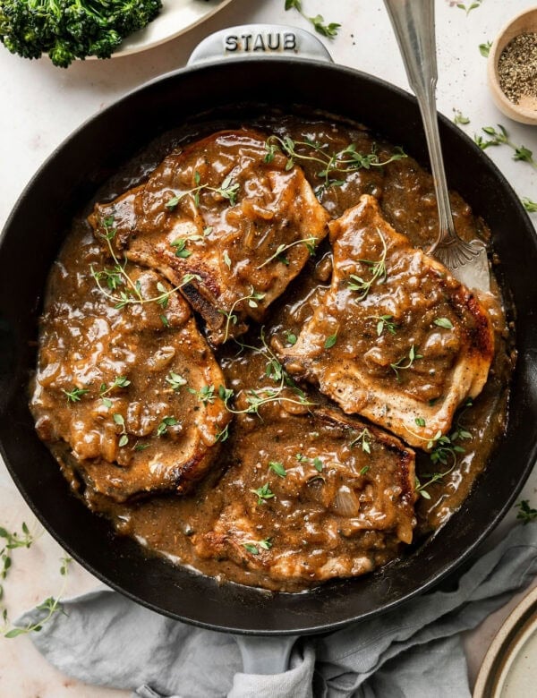Pork chops coated in gravy in a cast iron skillet