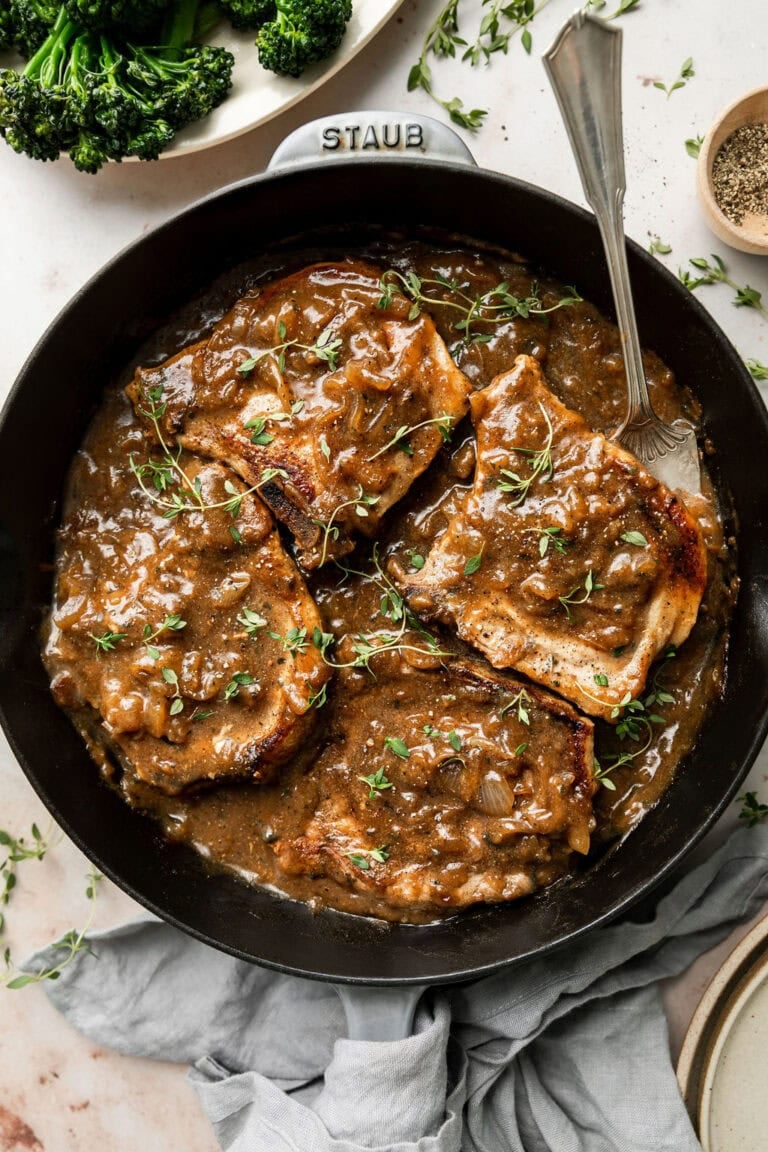 Overhead view of a cast iron skillet filled with smothered pork chops and rich brown gravy. 