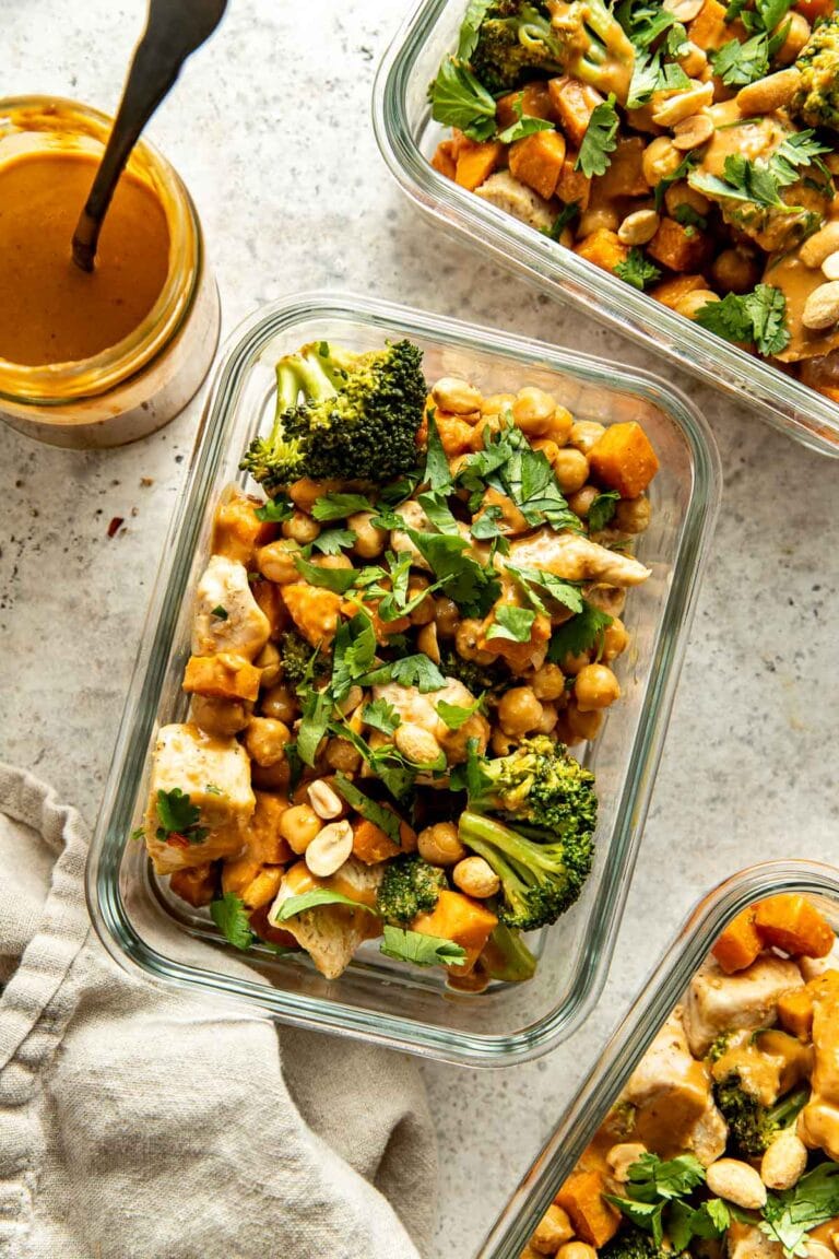 Overhead view of three glass meal prep containers filled with Thai peanut chicken bowls topped with cilantro and chopped peanuts.