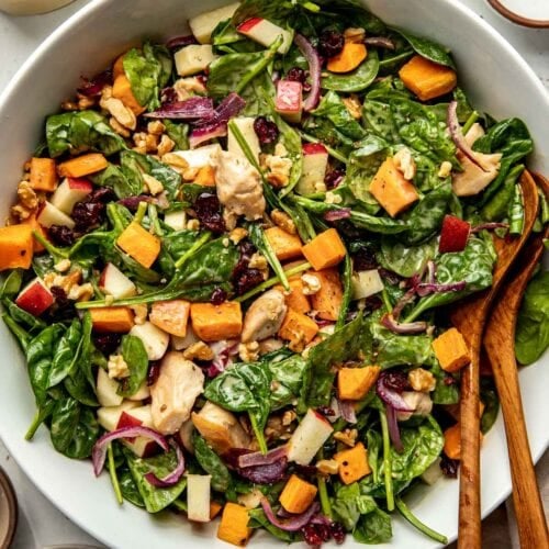 Overhead view white serving bowl filled with harvest chicken salad over spinach