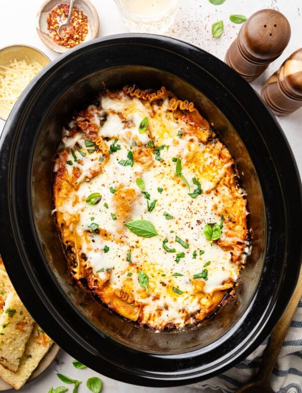 Overhead view lasagna in a crockpot, topped with melted cheese and fresh basil