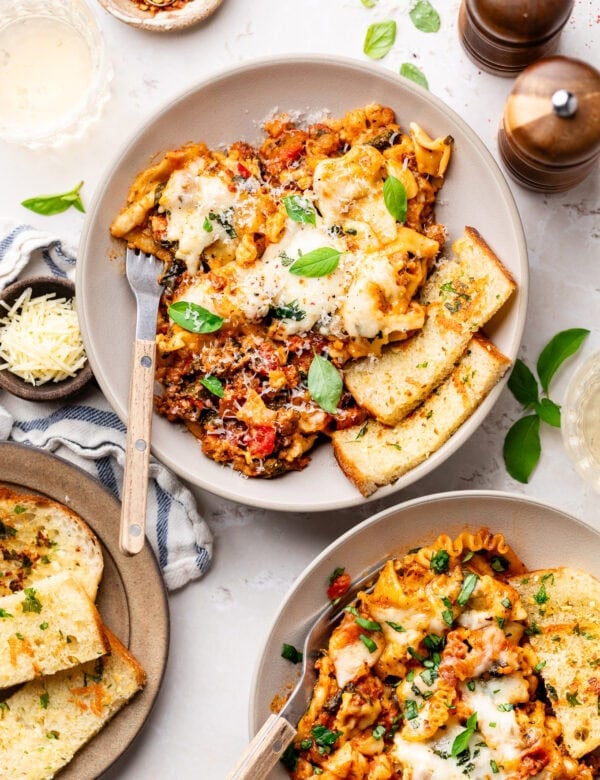 Overhead view two plates with servings of lasagna, garlic bread on the side.