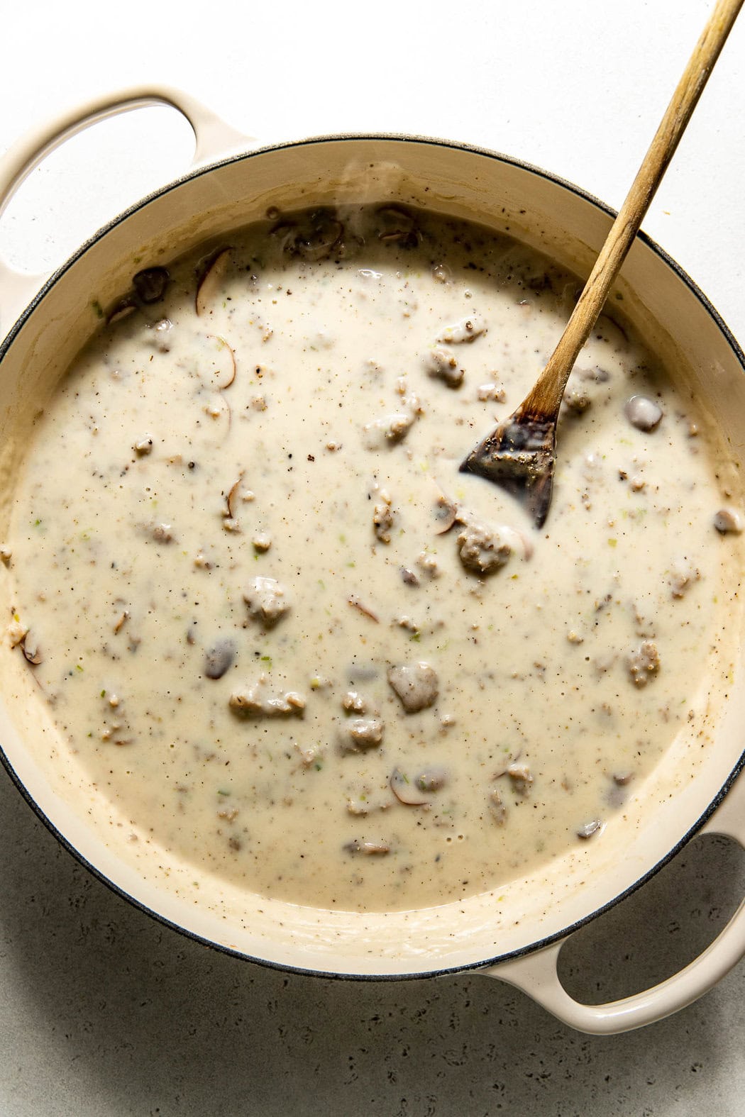Overhead view of a pan of sausage gravy with mushrooms and pork sausage thickening. 