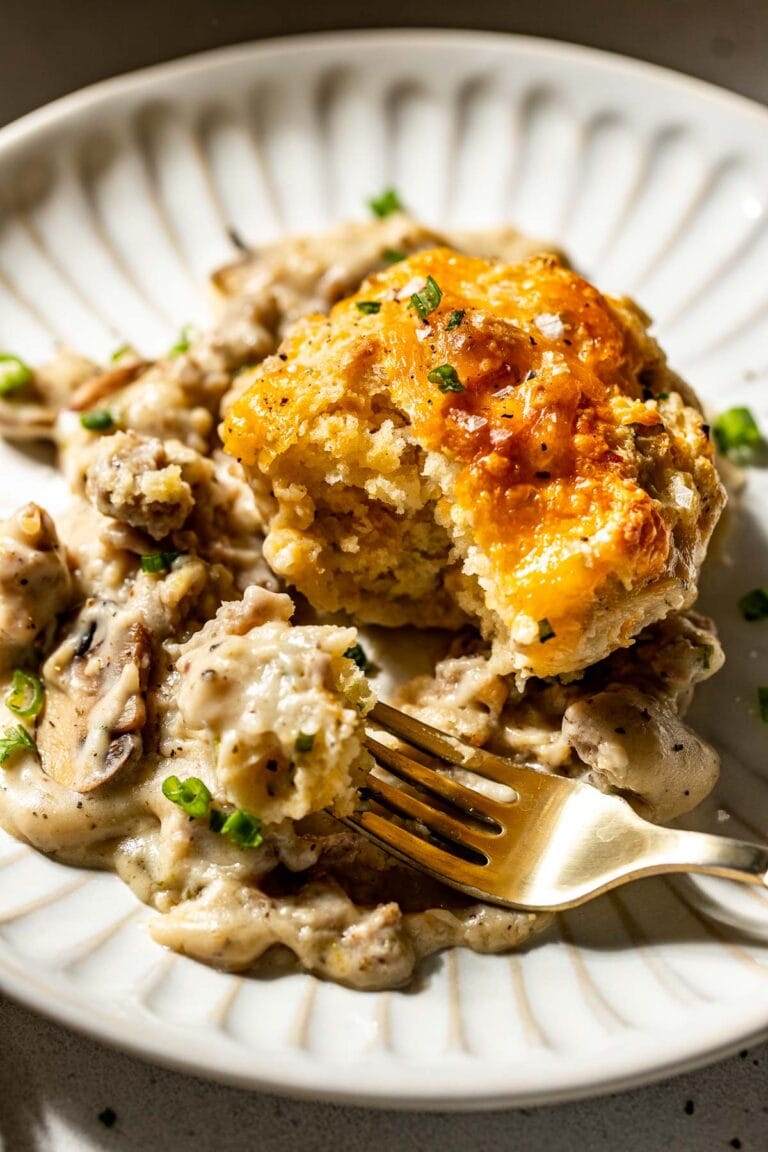 Close up view of a plate of biscuits and gravy casserole with a fork showing a bite dipped in the gravy. 