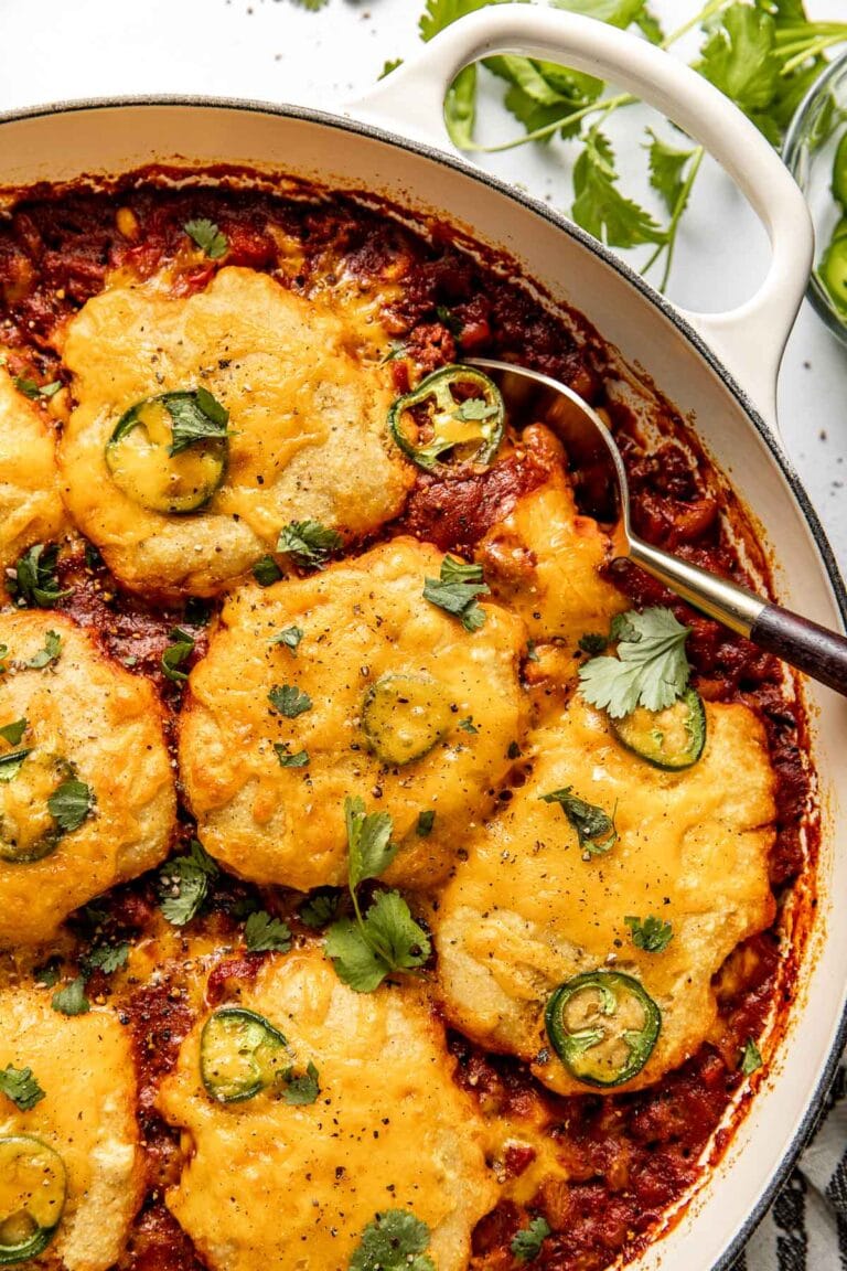 Overhead view of a skillet filled with chili cornbread casserole topped with sliced jalapenos and fresh herbs.
