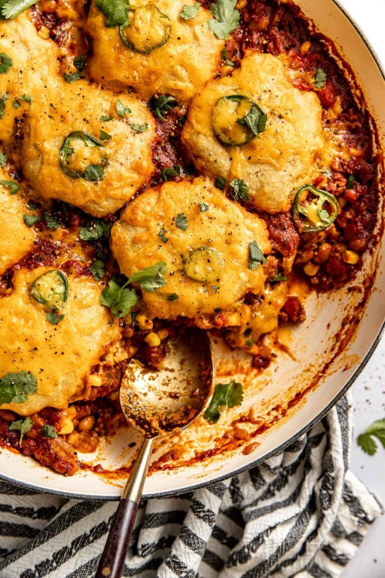 Overhead view of a baking dish filled with chili cornbread casserole topped with fresh herbs and black pepper. 