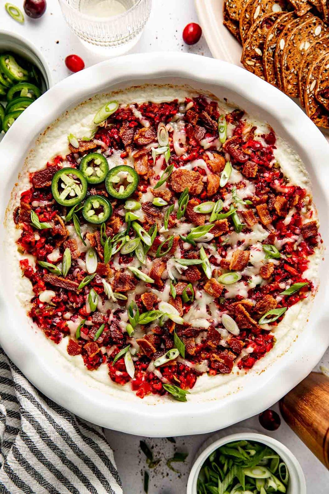 Overhead view of a freshly baked plate of Cranberry Jalapeño Dip (With Whipped Cottage Cheese) topped with crisp bacon and green onion.