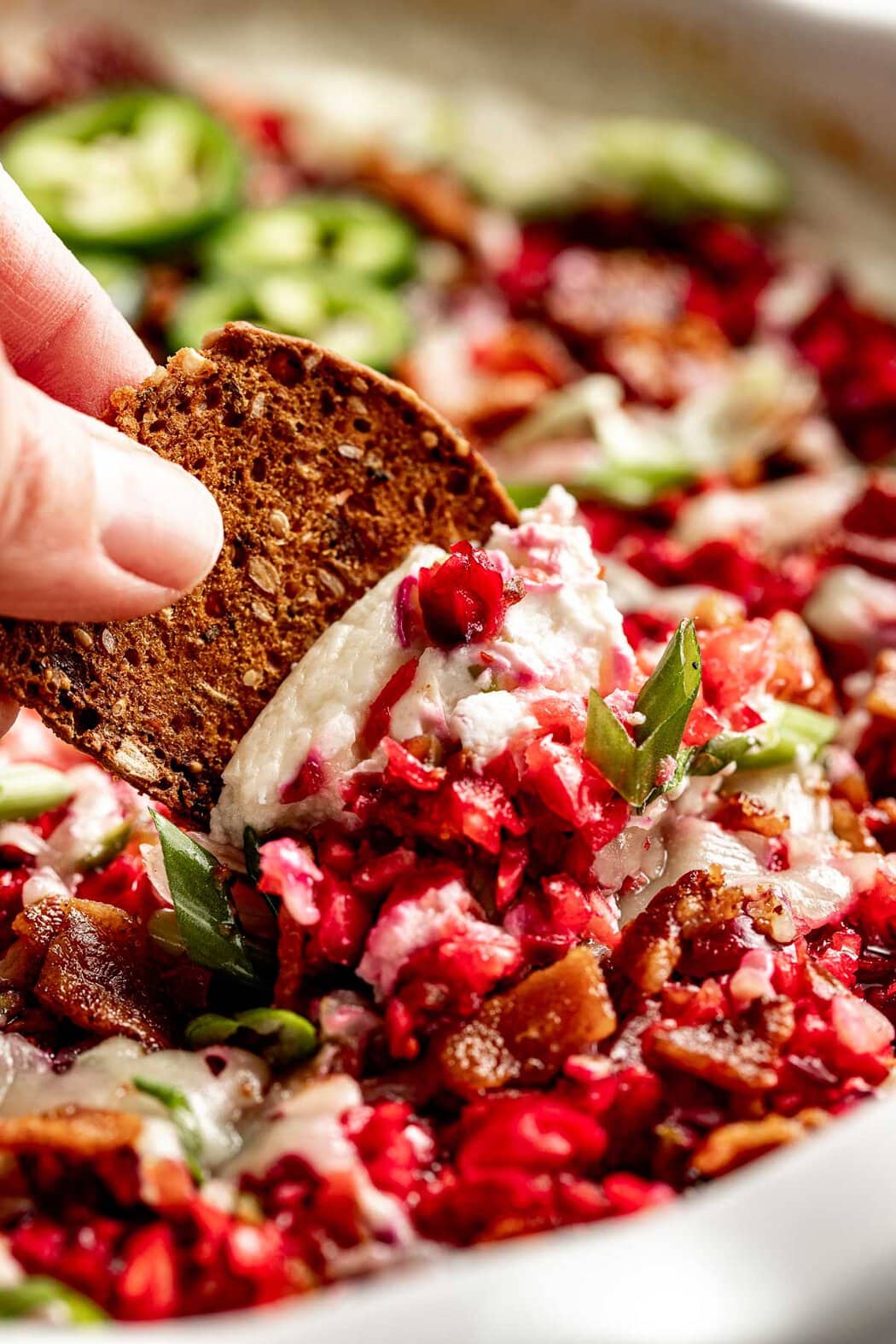 Close up view of a hand dipping a cracker into Cranberry Jalapeño Dip with Whipped Cottage Cheese.
