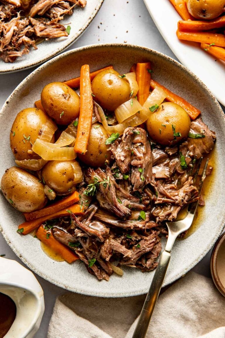 Overhead view of a plate of slow cooker pot roast with potatoes and carrots on the side and all topped with brown gravy.