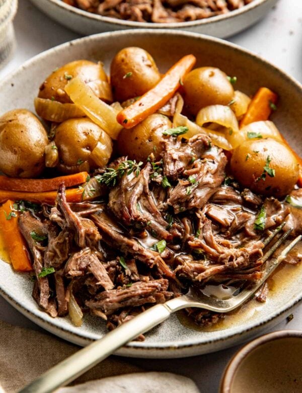 Side view of shredded pot roast served in a bowl with baby potatoes and carrots