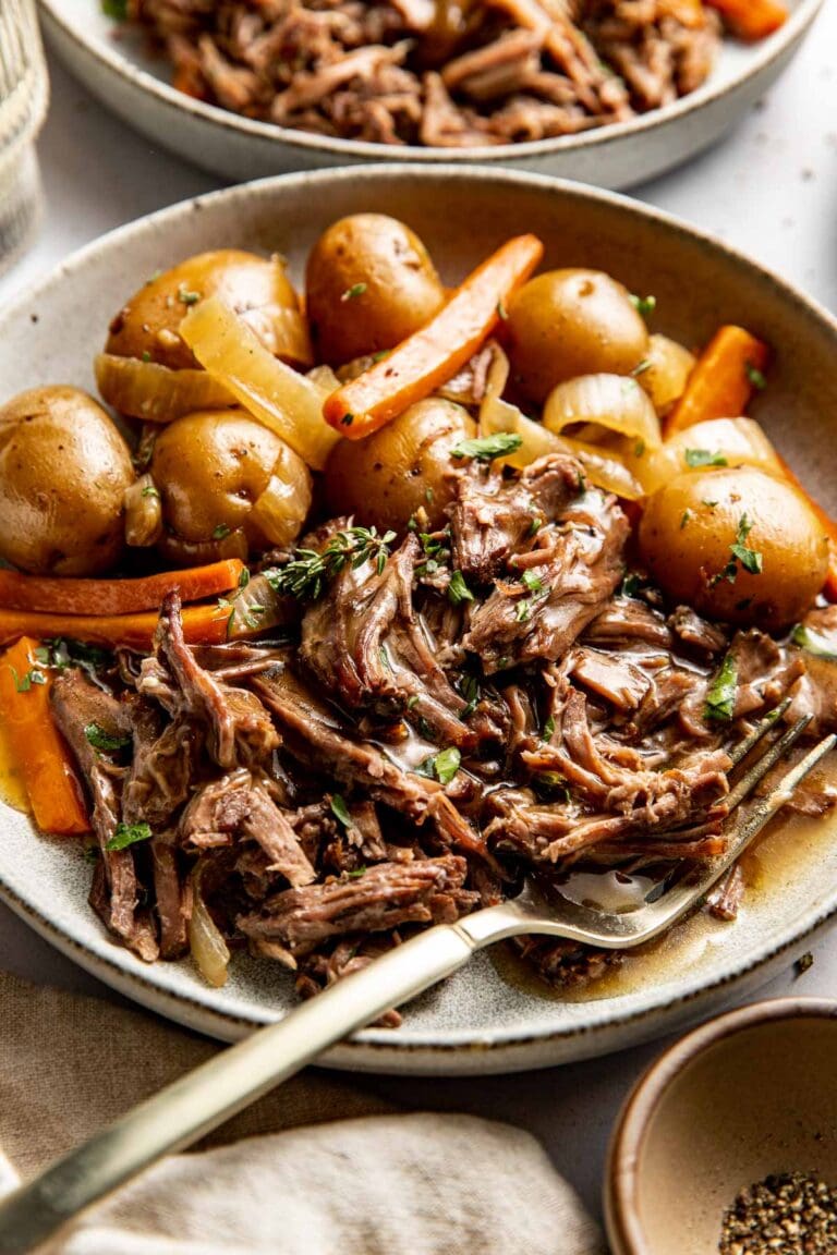 Close up view of a plate filled with slow cooker pot roast with carrots and potatoes. 
