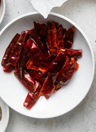 A small white bowl filled with dried guajillo peppers.