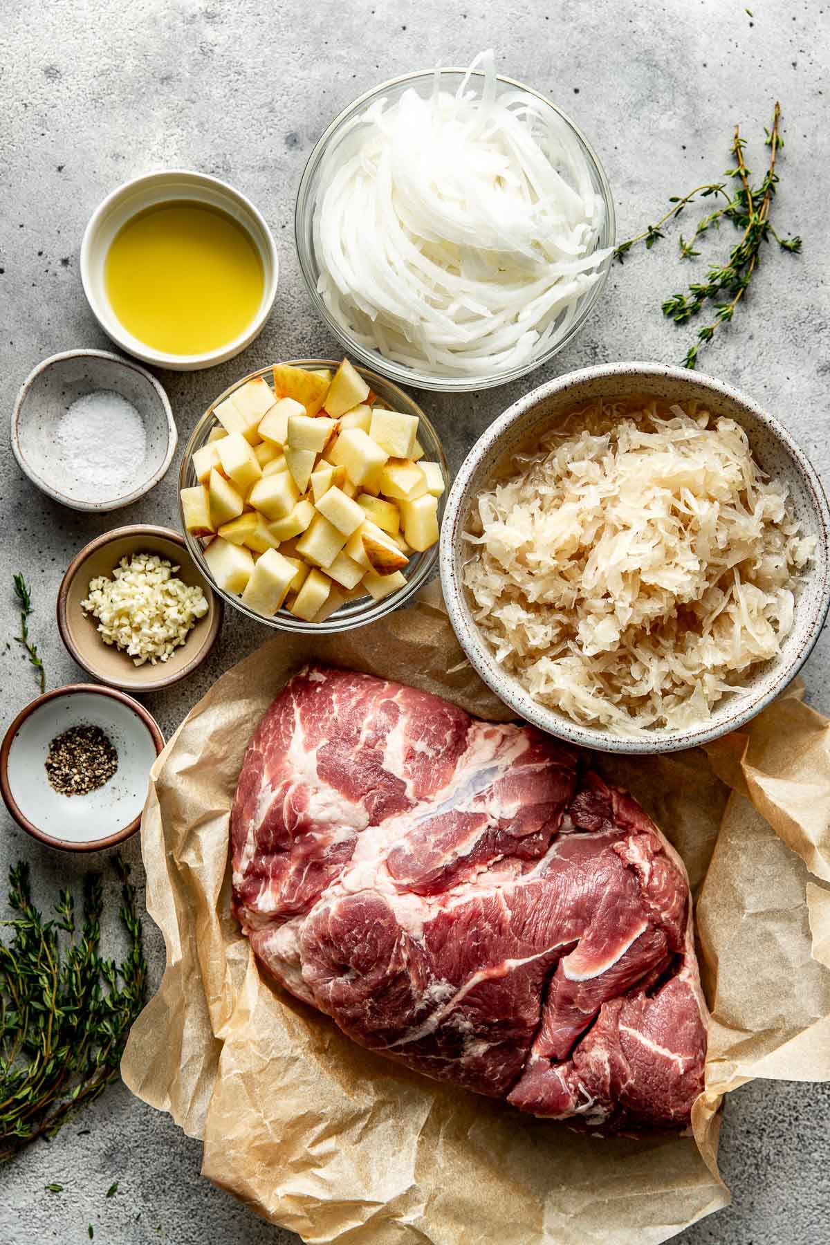 Overhead view of a variety of ingredients for Pork And Sauerkraut in different sized bowls. 