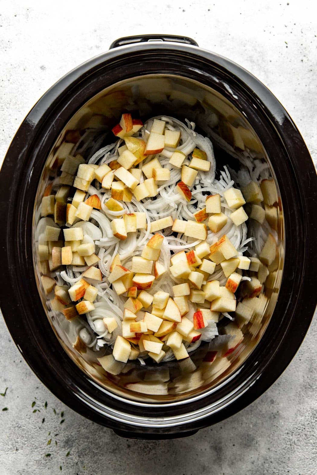 Overhead view of a crockpot filled with sliced onions and apple pieces. 