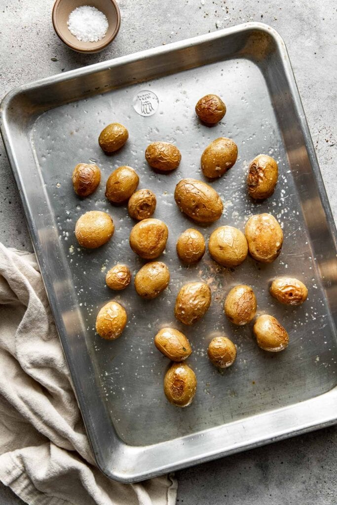 Overhead view of a sheet pan of Roasted Baby Potatoes topped with flakey sea salt. 