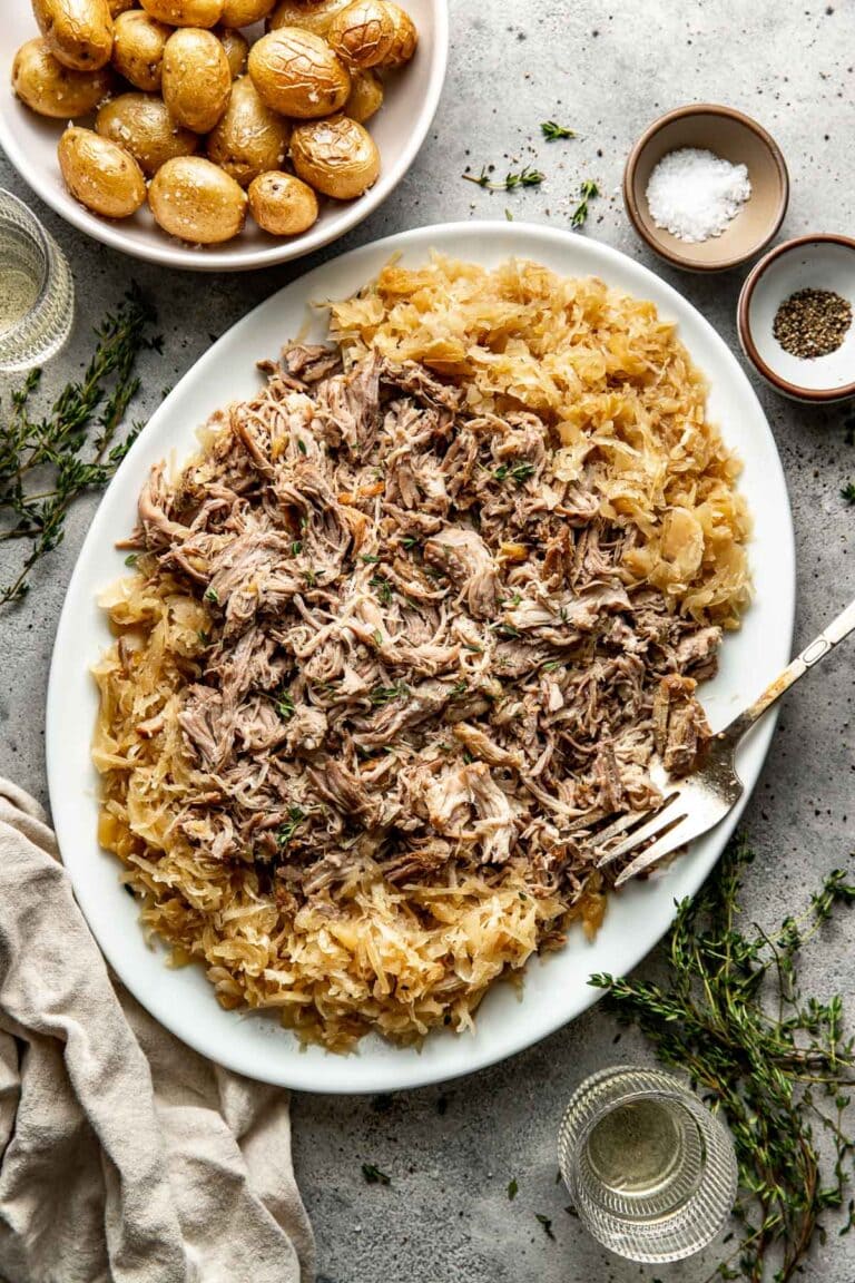 Overhead view of a platter filled with crockpot pork and sauerkraut topped with fresh herbs. 
