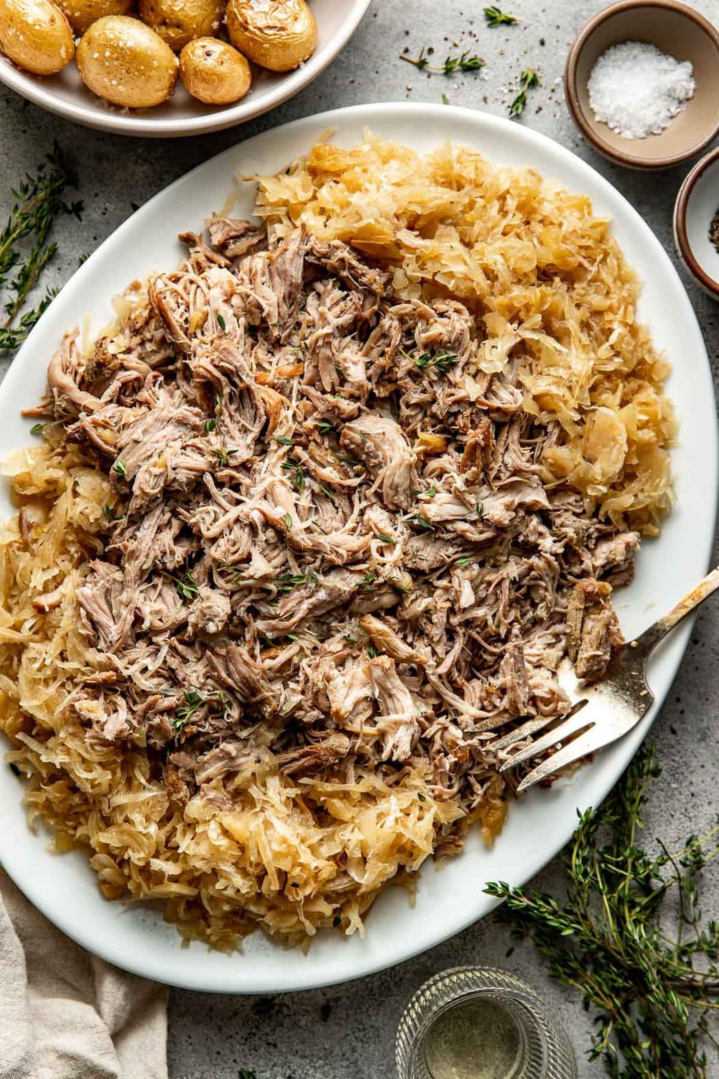 Overhead view of a platter filled with freshly cooked Pork And Sauerkraut (In The Crockpot) topped with fresh thyme. 