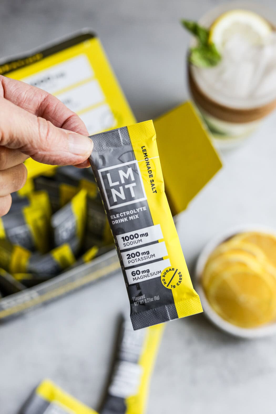 Close up view of a hand holding a packet of lemon salt LMNT electrolyte mix. 