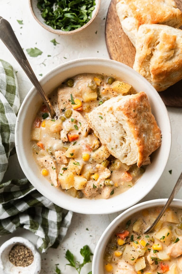Overhead view of two bowls of chicken pot pie soup with a homemade biscuit dipped into the side of the bowl.