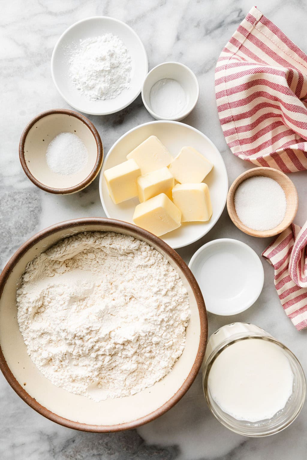 Overhead view of a variety of ingredients for homemade biscuits in different sized bowls. 