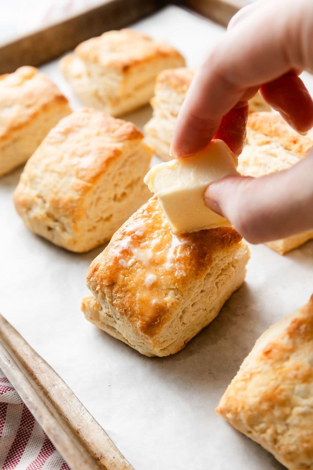 Close up view of a hand spreading butter over freshly baked biscuits. 