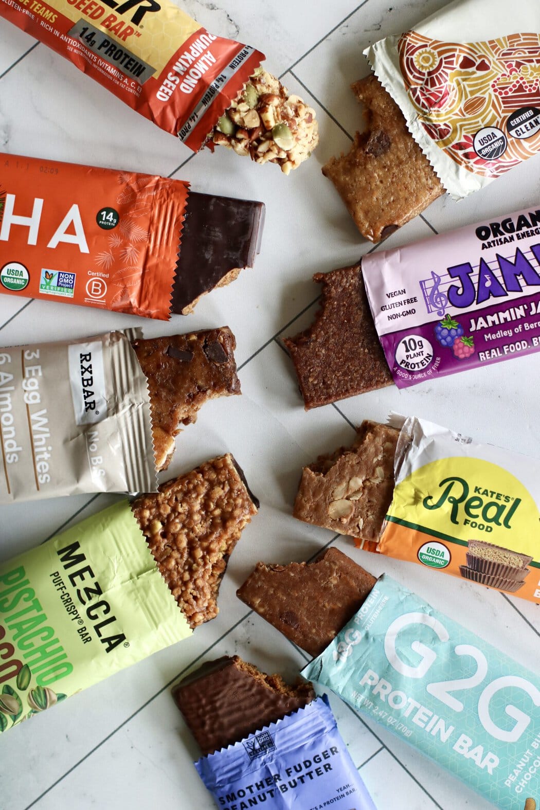 Overhead view of several opened protein bars arranged on a white marble countertop all showing the texture and color of the bars.